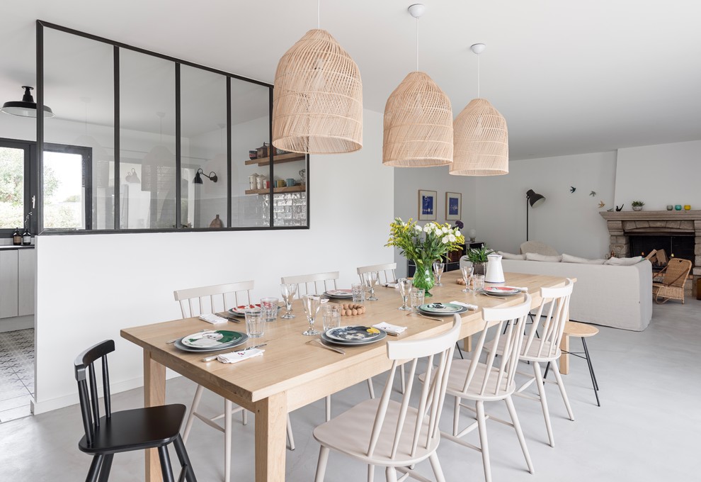 Medium sized scandinavian dining room with white walls, concrete flooring, a standard fireplace, a stone fireplace surround and grey floors.