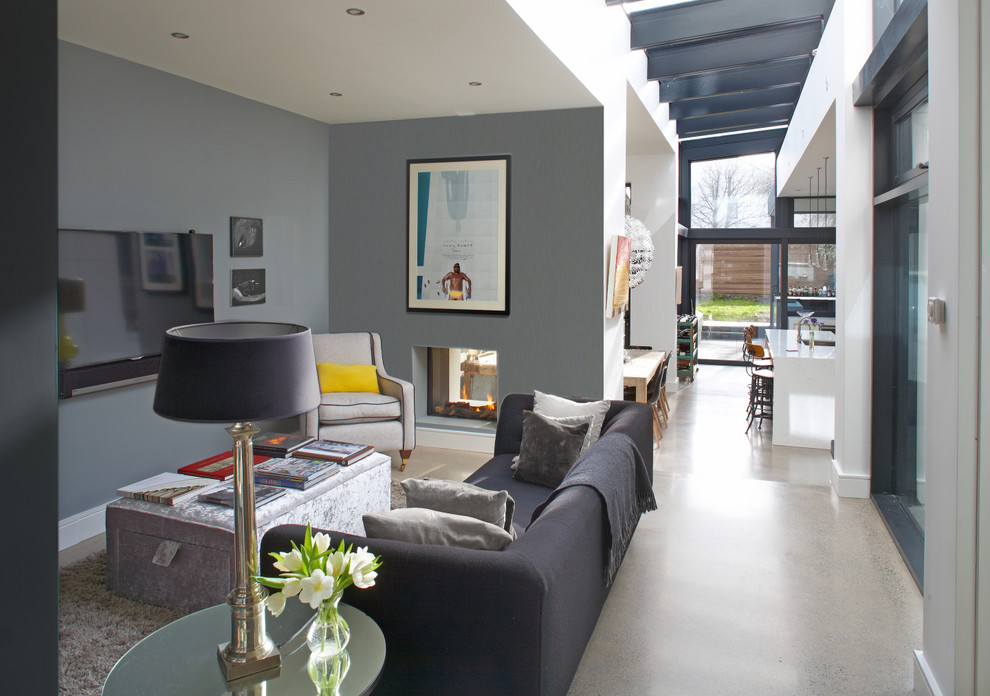 Cette image montre un salon design ouvert avec un mur gris, sol en béton ciré, un téléviseur fixé au mur et canapé noir.