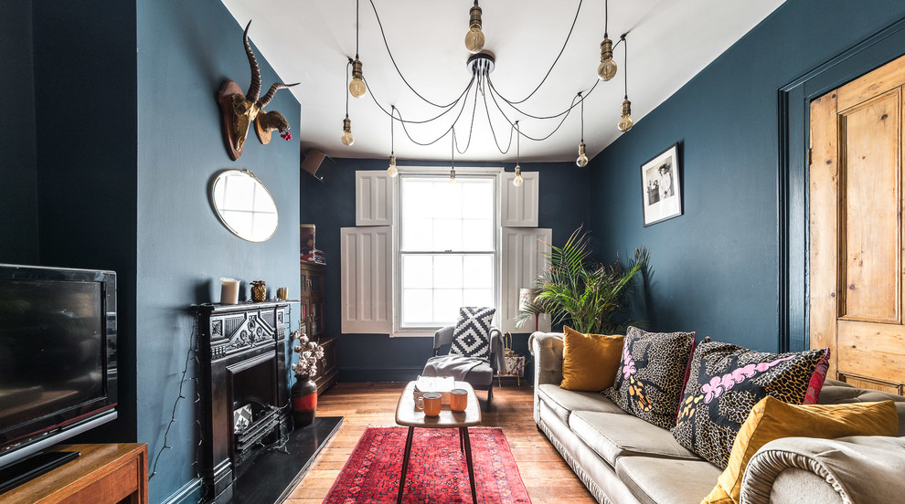 Modelo de salón cerrado bohemio de tamaño medio con paredes azules, todas las chimeneas, televisor independiente, suelo marrón y suelo de madera en tonos medios