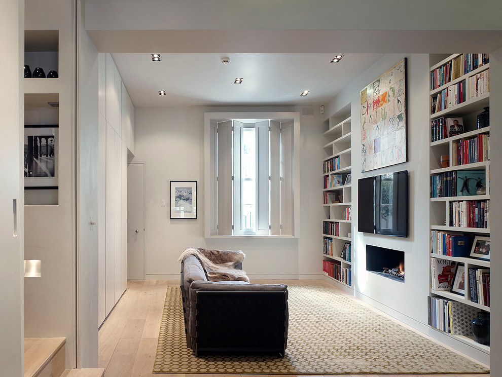 Skandinavisk inredning av ett separat vardagsrum, med vita väggar, en väggmonterad TV, ett bibliotek, ljust trägolv och en standard öppen spis