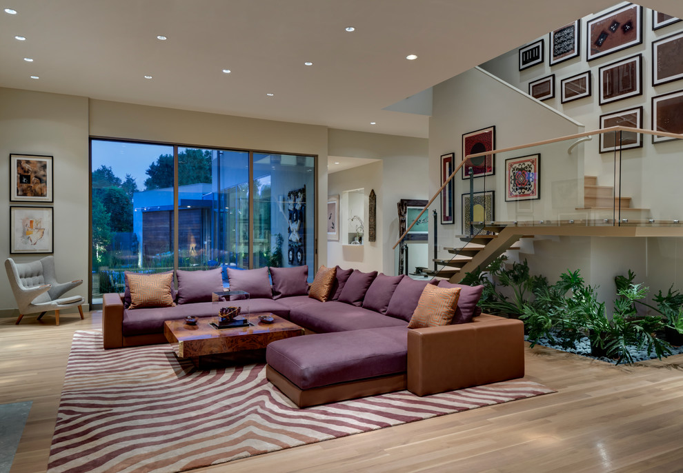 This is an example of a large modern open plan living room in Dallas with beige walls and light hardwood flooring.