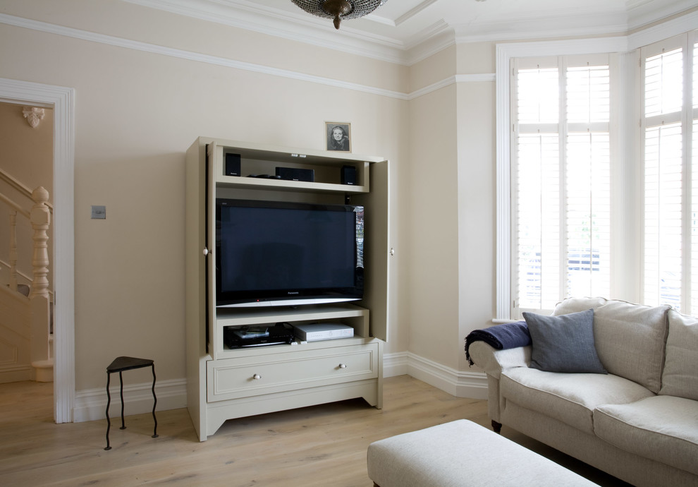 Diseño de salón cerrado tradicional de tamaño medio con paredes beige, suelo de madera clara y televisor retractable