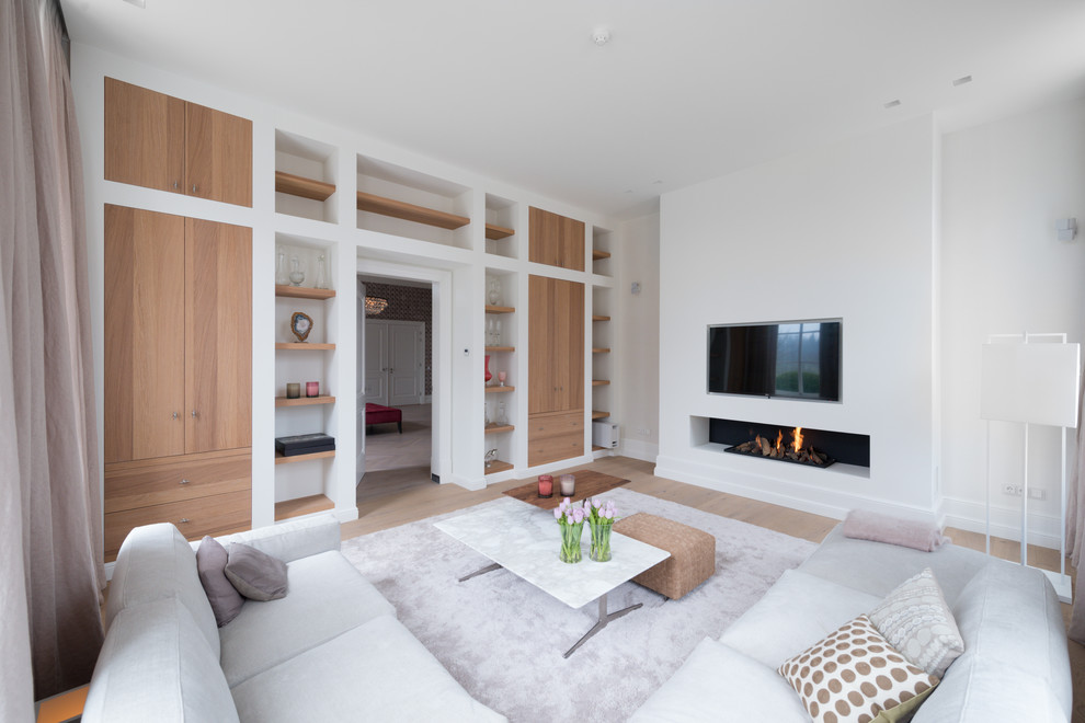 Inspiration för minimalistiska separata vardagsrum, med ett finrum, vita väggar, ljust trägolv, en bred öppen spis, en spiselkrans i gips och en väggmonterad TV