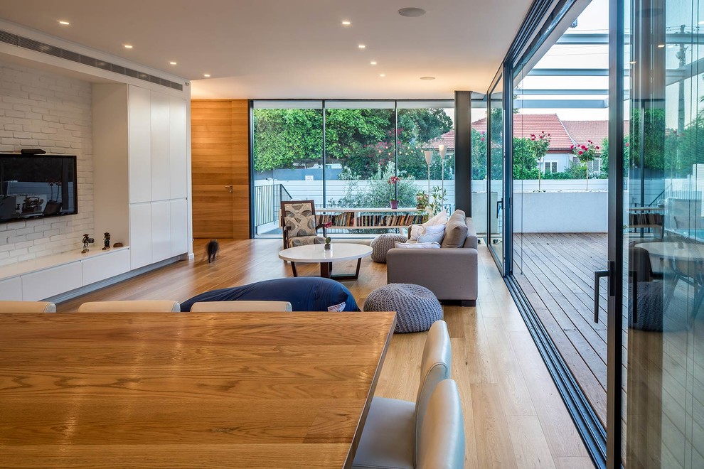 Small modern formal open plan living room in Tel Aviv with white walls, light hardwood flooring and a wall mounted tv.