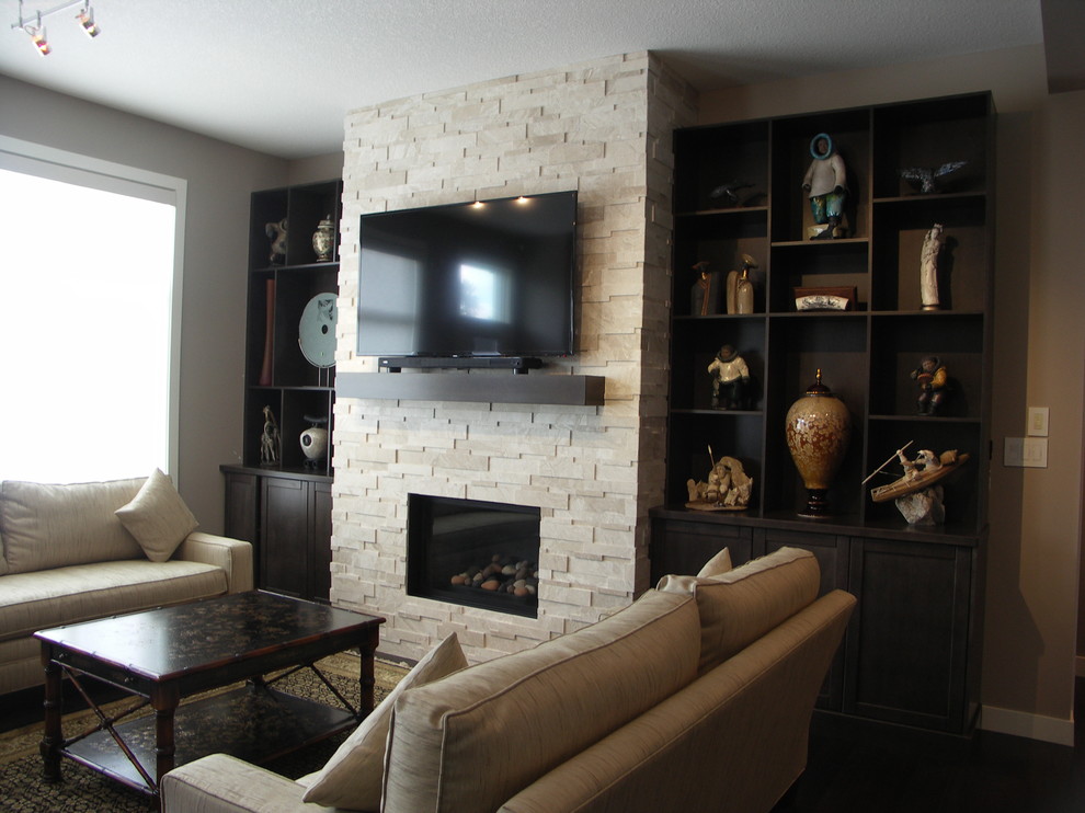 Mittelgroßes, Abgetrenntes Modernes Wohnzimmer mit grauer Wandfarbe, dunklem Holzboden, Kamin, Kaminumrandung aus Stein, freistehendem TV und braunem Boden in Edmonton