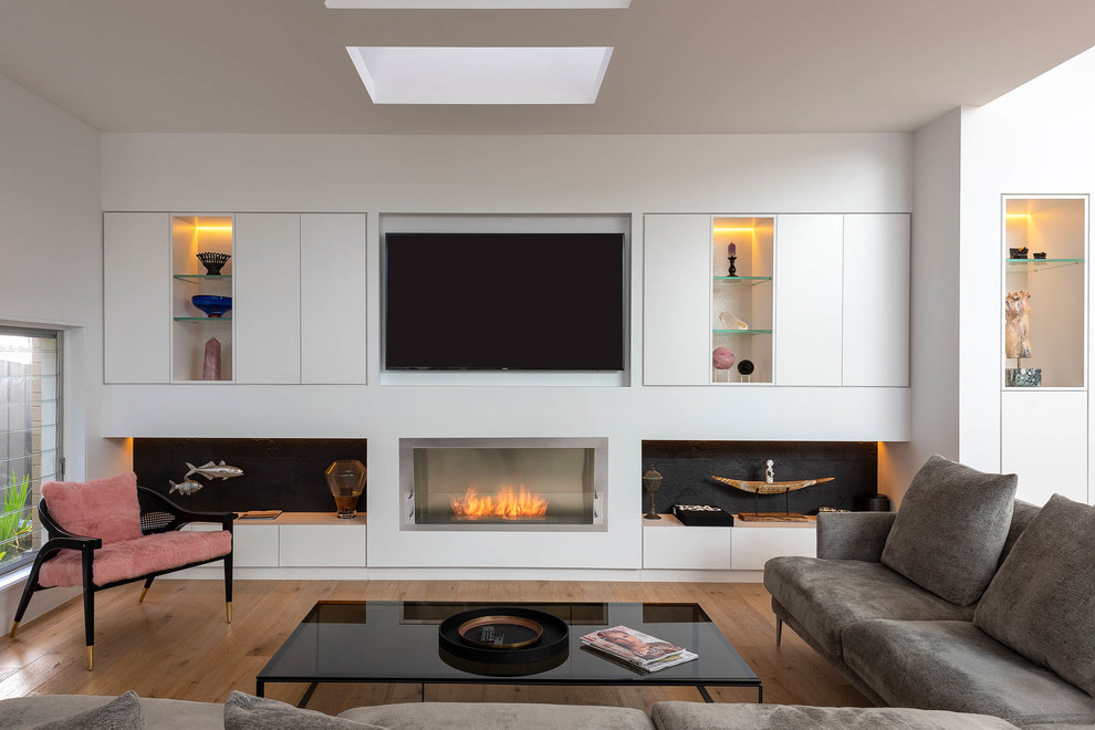 This is an example of a large contemporary open plan living room in Sydney with white walls, light hardwood flooring, a standard fireplace, a plastered fireplace surround and a built-in media unit.