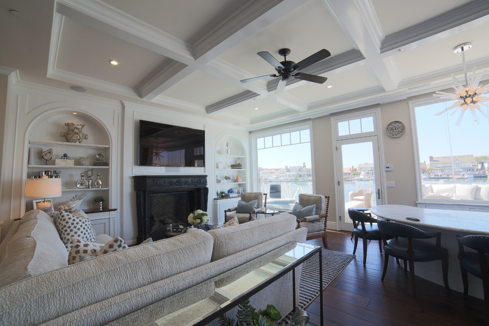 This is an example of a large coastal open plan living room in Orange County with a reading nook, dark hardwood flooring, a two-sided fireplace, a plastered fireplace surround, a wall mounted tv and brown floors.