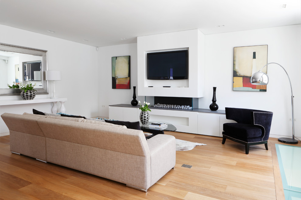 Стильный дизайн: изолированная гостиная комната среднего размера в современном стиле с белыми стенами, светлым паркетным полом, горизонтальным камином, телевизором на стене и бежевым полом - последний тренд