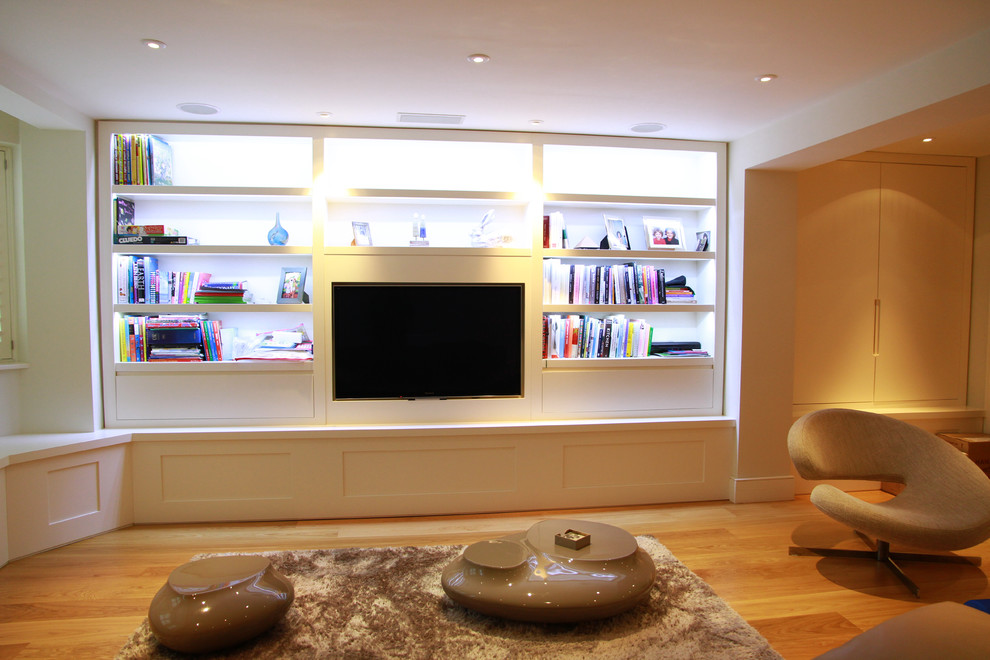 This is an example of a small modern enclosed living room in London with a reading nook, white walls, light hardwood flooring, no fireplace and a built-in media unit.
