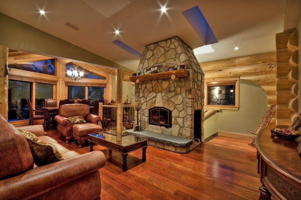 Exemple d'un salon chic ouvert avec un mur vert, un sol en bois brun, un poêle à bois, un manteau de cheminée en pierre, aucun téléviseur et un sol marron.