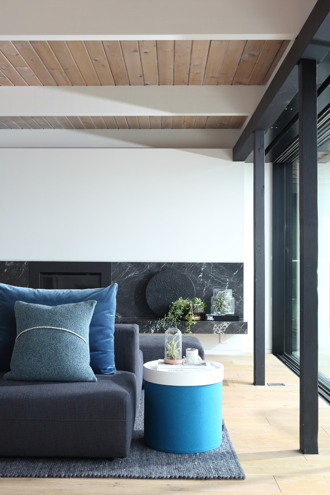 Mittelgroßes, Fernseherloses, Offenes Retro Wohnzimmer mit weißer Wandfarbe, hellem Holzboden, Kamin und Kaminumrandung aus Stein in Vancouver