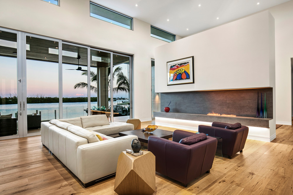 Идея дизайна: большая открытая гостиная комната в современном стиле с белыми стенами, светлым паркетным полом, горизонтальным камином, фасадом камина из бетона, скрытым телевизором и коричневым полом