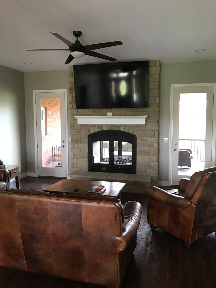 This is an example of a large romantic formal enclosed living room in Kansas City with beige walls, dark hardwood flooring, a two-sided fireplace, a stone fireplace surround, a wall mounted tv and brown floors.