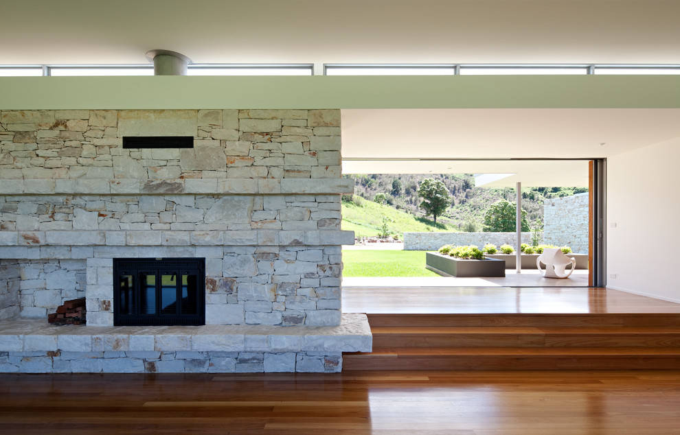 Imagen de salón abierto minimalista grande con paredes verdes, suelo de madera en tonos medios, todas las chimeneas, marco de chimenea de piedra y televisor colgado en la pared