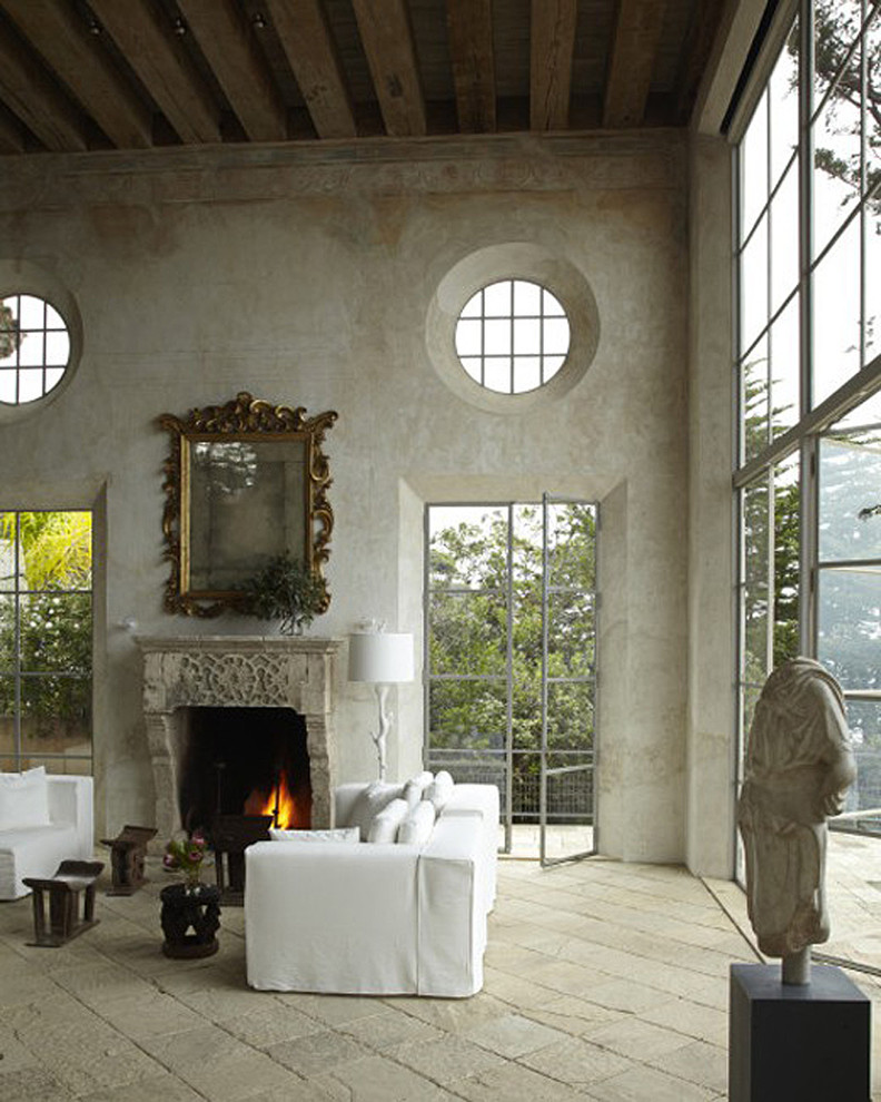 Стильный дизайн: большая парадная, открытая гостиная комната в средиземноморском стиле с полом из известняка, стандартным камином, фасадом камина из камня и серыми стенами без телевизора - последний тренд