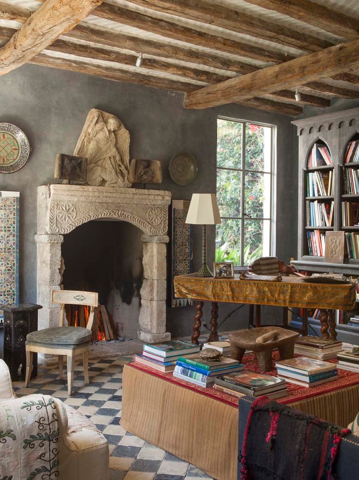 Exemple d'un grand salon méditerranéen ouvert avec un sol en calcaire, une cheminée standard, un manteau de cheminée en pierre, une bibliothèque ou un coin lecture, un mur gris et aucun téléviseur.