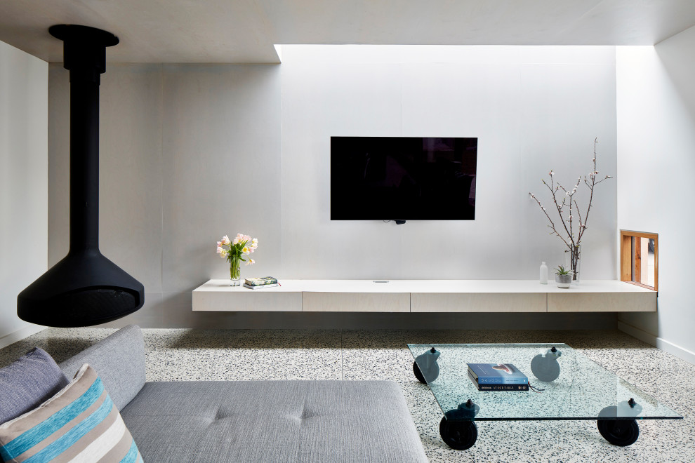 На фото: большая открытая гостиная комната в современном стиле с белыми стенами, бетонным полом, подвесным камином, телевизором на стене и серым полом