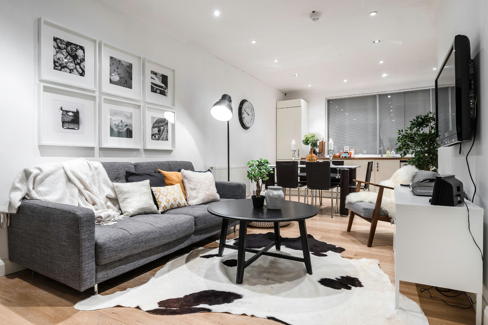 Scandi open plan living room in London with white walls, light hardwood flooring and a wall mounted tv.