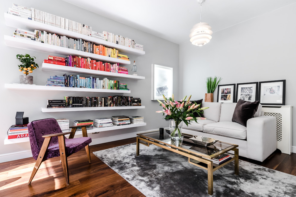 Cette photo montre un salon chic avec une bibliothèque ou un coin lecture, un mur gris et un sol en bois brun.