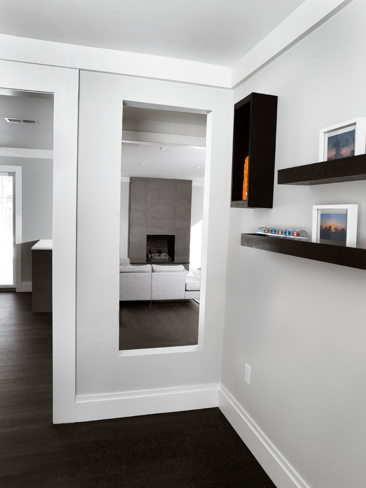 Modelo de salón abierto minimalista grande con paredes grises, suelo de madera oscura, todas las chimeneas, marco de chimenea de piedra y televisor colgado en la pared