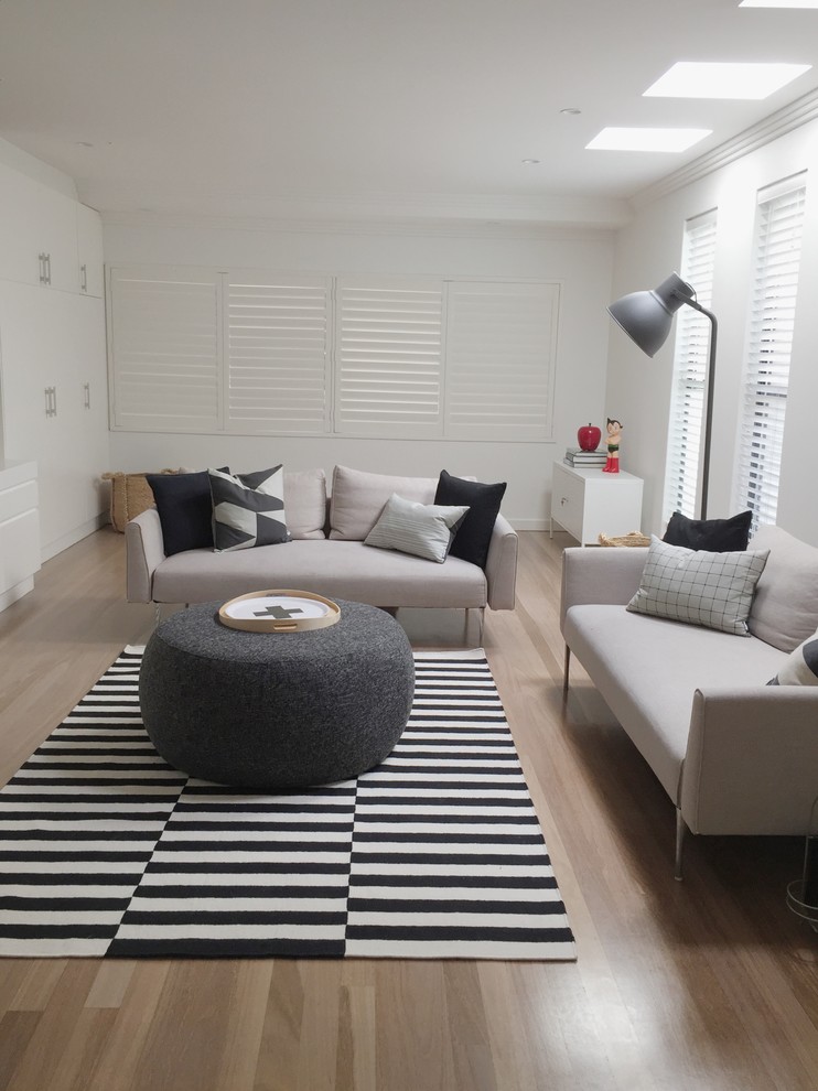 Diseño de salón abierto nórdico grande con paredes blancas, suelo de madera clara, televisor independiente y suelo beige