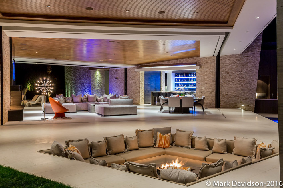 На фото: огромная открытая гостиная комната в стиле модернизм с разноцветными стенами, стандартным камином, фасадом камина из камня и телевизором на стене