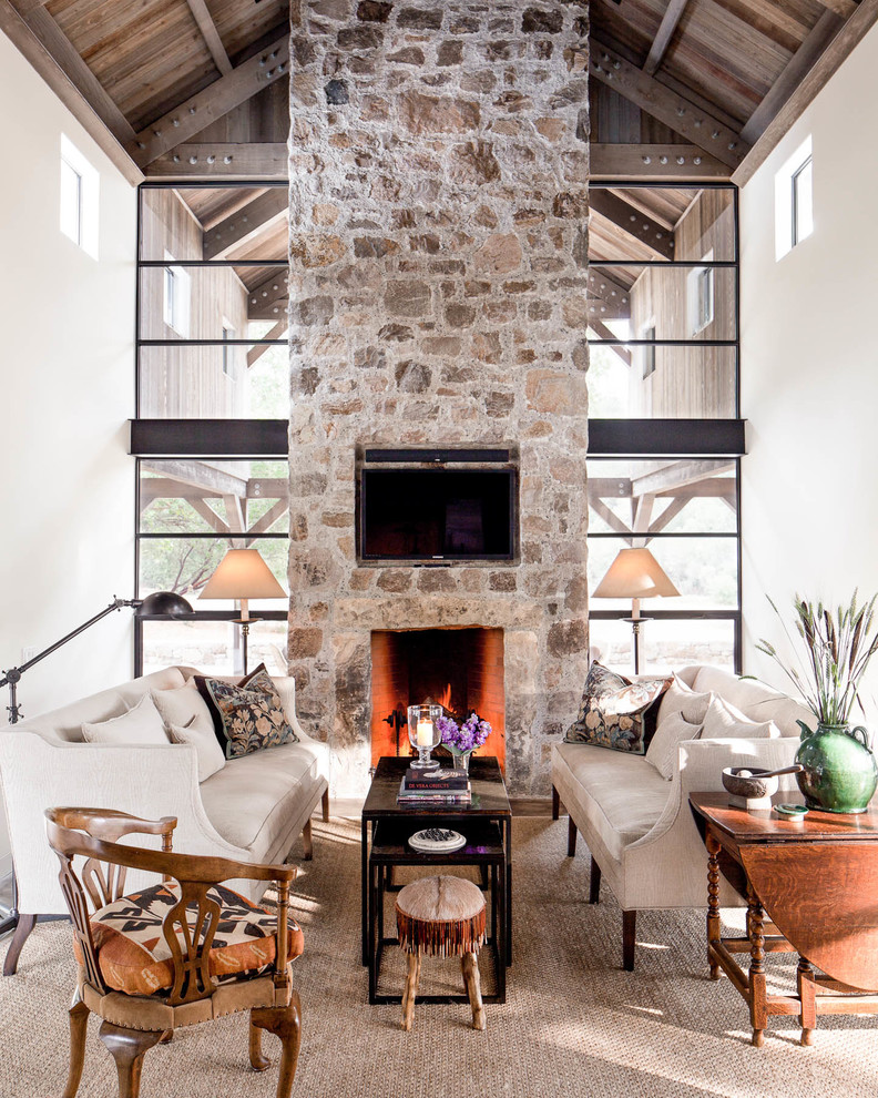This is an example of a rural living room in San Francisco with white walls, a standard fireplace, a stone fireplace surround, a wall mounted tv and beige floors.
