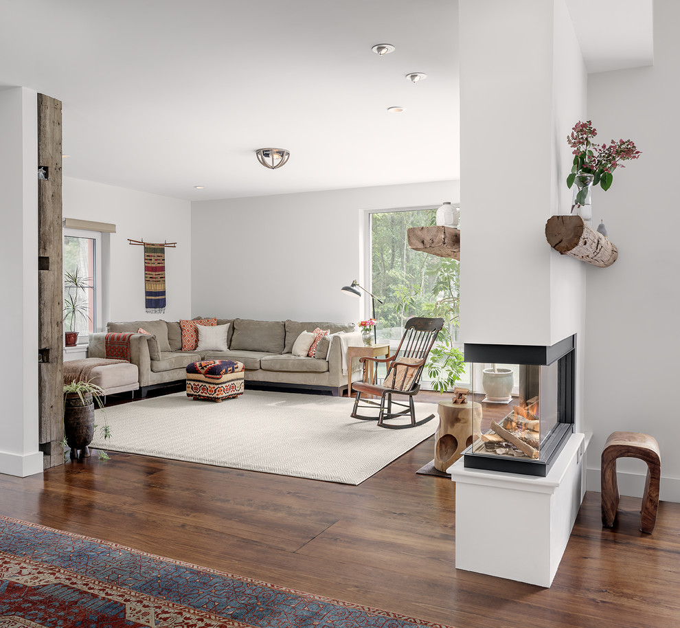 Ejemplo de salón abierto con paredes blancas, suelo de madera oscura, chimenea de doble cara y suelo marrón