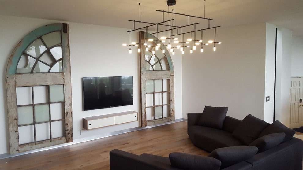 Modelo de salón abierto minimalista extra grande con paredes blancas, suelo de madera clara, todas las chimeneas, marco de chimenea de piedra y televisor colgado en la pared