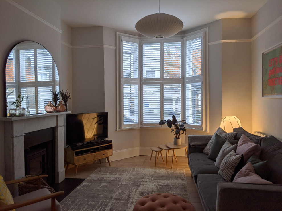 This is an example of a medium sized scandi open plan living room in London with white walls, painted wood flooring, a wood burning stove, a stone fireplace surround and white floors.