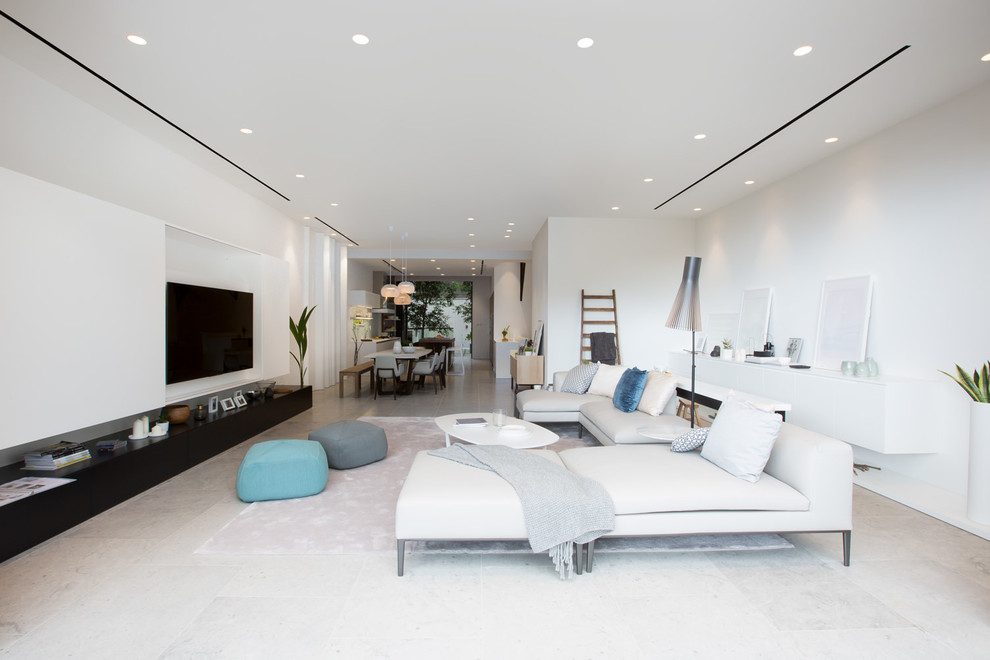 Aménagement d'un salon moderne avec un mur blanc, un sol en calcaire et un téléviseur encastré.