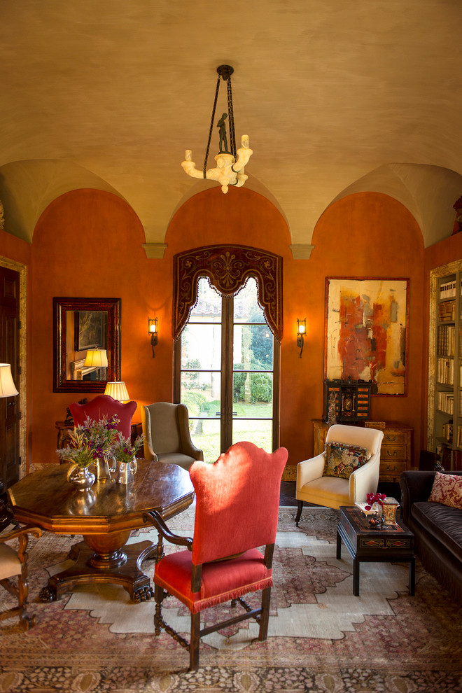 Стильный дизайн: большая изолированная гостиная комната в средиземноморском стиле с с книжными шкафами и полками, оранжевыми стенами, темным паркетным полом, стандартным камином и фасадом камина из камня - последний тренд