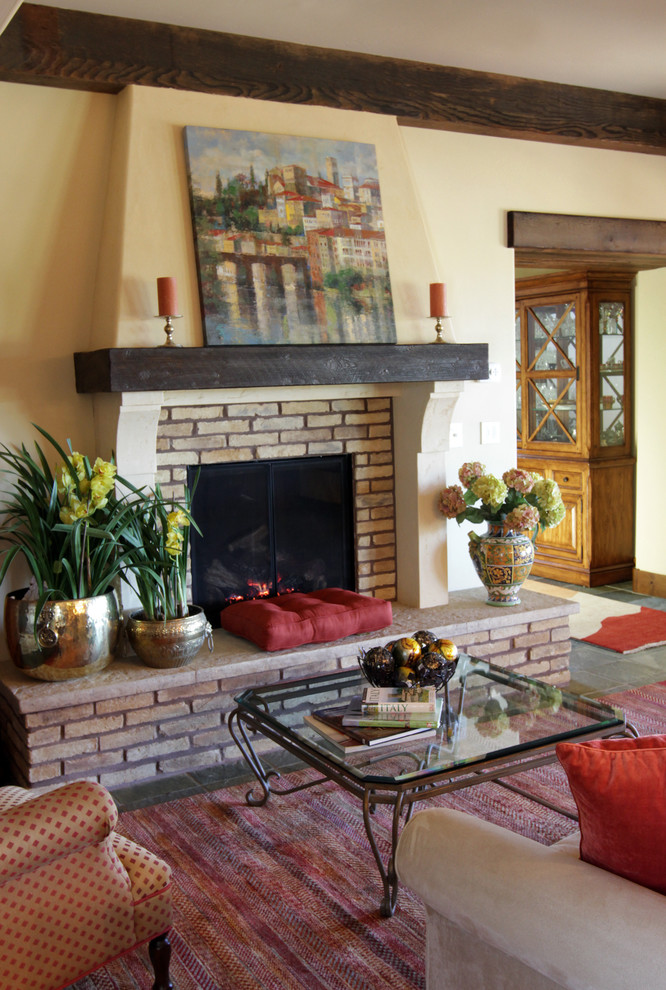 Cette image montre un grand salon méditerranéen ouvert avec une salle de réception, un mur beige, un sol en ardoise, une cheminée standard, un manteau de cheminée en brique et un téléviseur dissimulé.