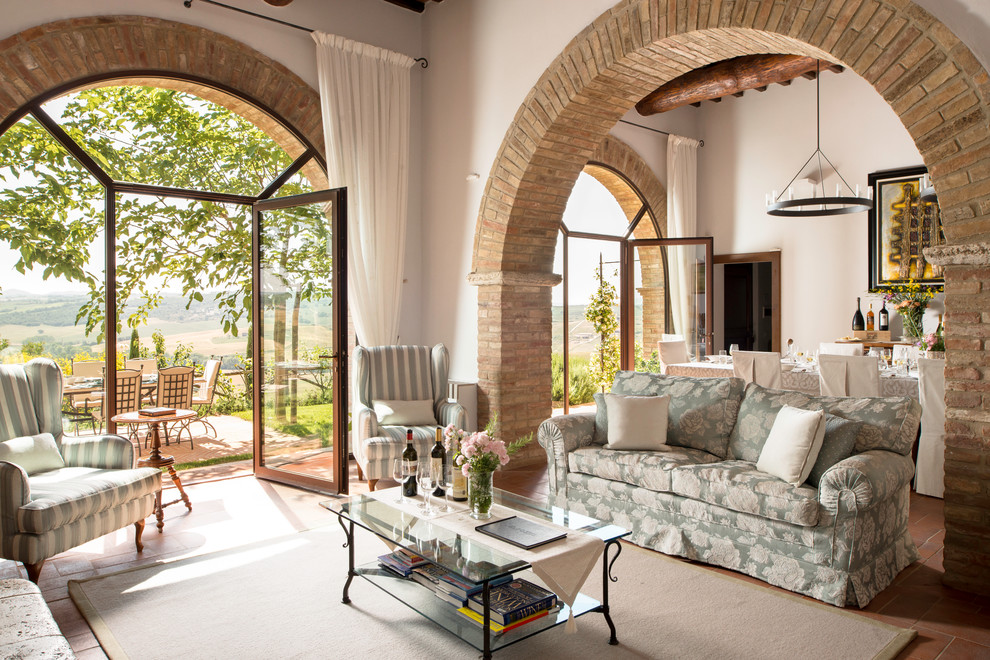 Стильный дизайн: парадная, открытая гостиная комната в средиземноморском стиле с белыми стенами, полом из терракотовой плитки и ковром на полу - последний тренд