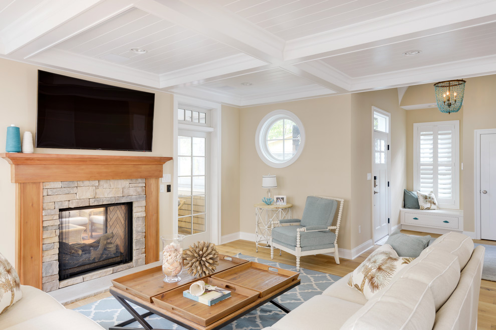 Imagen de salón abierto marinero con paredes beige, suelo de madera clara, chimenea de doble cara, marco de chimenea de piedra y televisor colgado en la pared