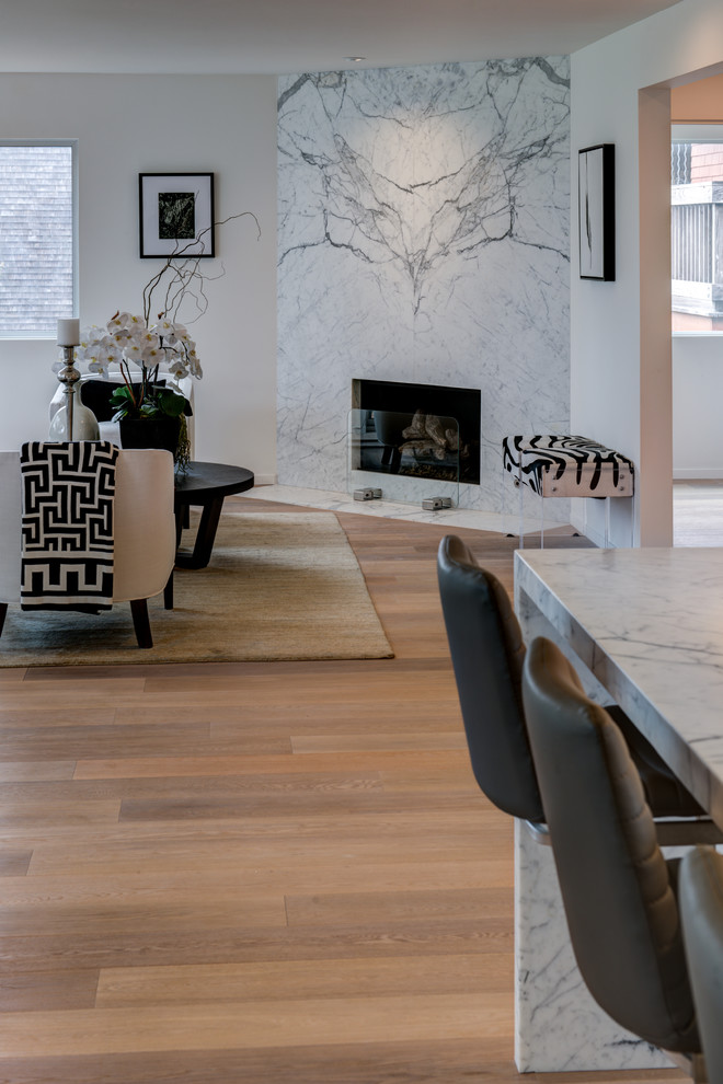 Modelo de salón abierto actual de tamaño medio con paredes blancas, suelo de madera en tonos medios, chimenea de esquina y marco de chimenea de piedra