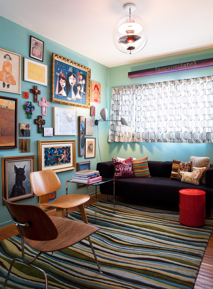 Cette image montre un salon bohème avec un mur bleu, un sol en bois brun et canapé noir.