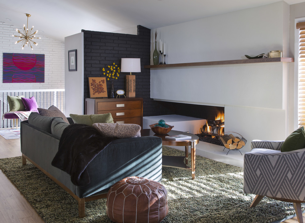 デンバーにある中くらいなミッドセンチュリースタイルのおしゃれなLDK (白い壁、無垢フローリング、標準型暖炉、漆喰の暖炉まわり、茶色い床) の写真
