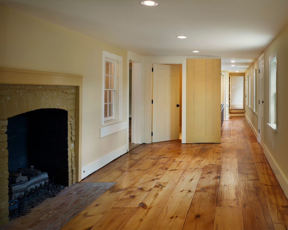 Klassisk inredning av ett mellanstort vardagsrum, med gula väggar, mellanmörkt trägolv, en standard öppen spis, en spiselkrans i trä och brunt golv