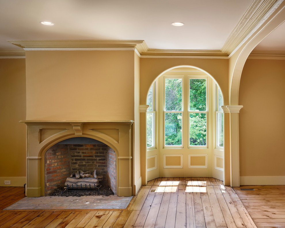 Idée de décoration pour un salon tradition de taille moyenne avec un mur jaune, un sol en bois brun, une cheminée standard, un manteau de cheminée en bois et un sol marron.
