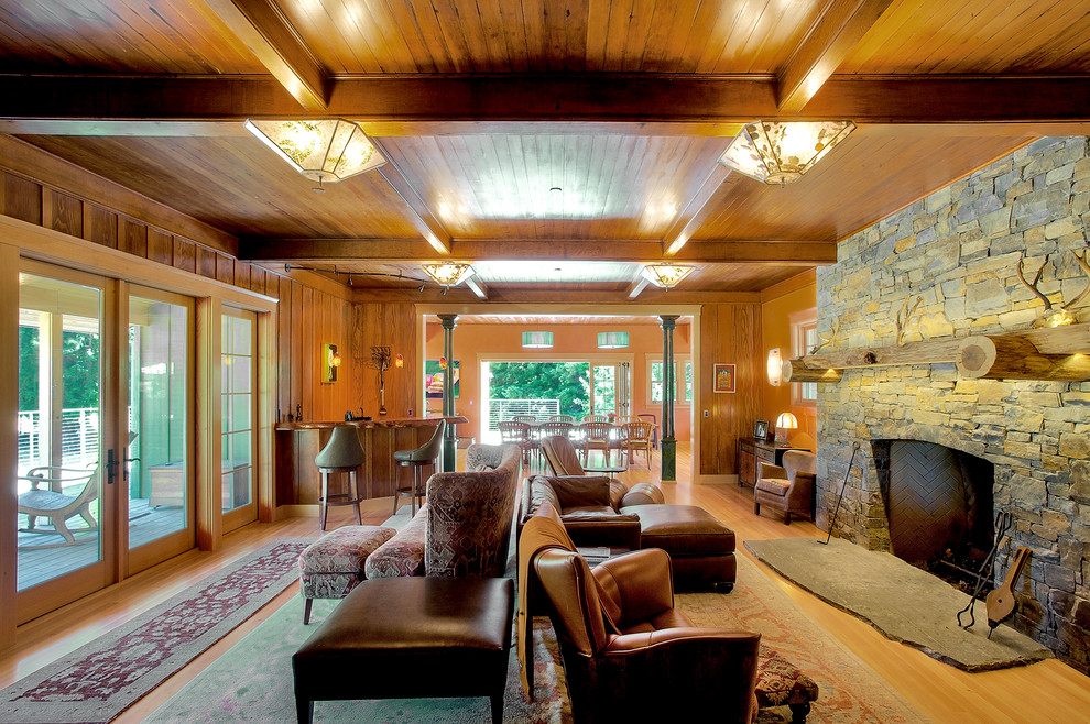 Пример оригинального дизайна: большая открытая гостиная комната в стиле кантри с домашним баром, светлым паркетным полом, стандартным камином и фасадом камина из камня без телевизора