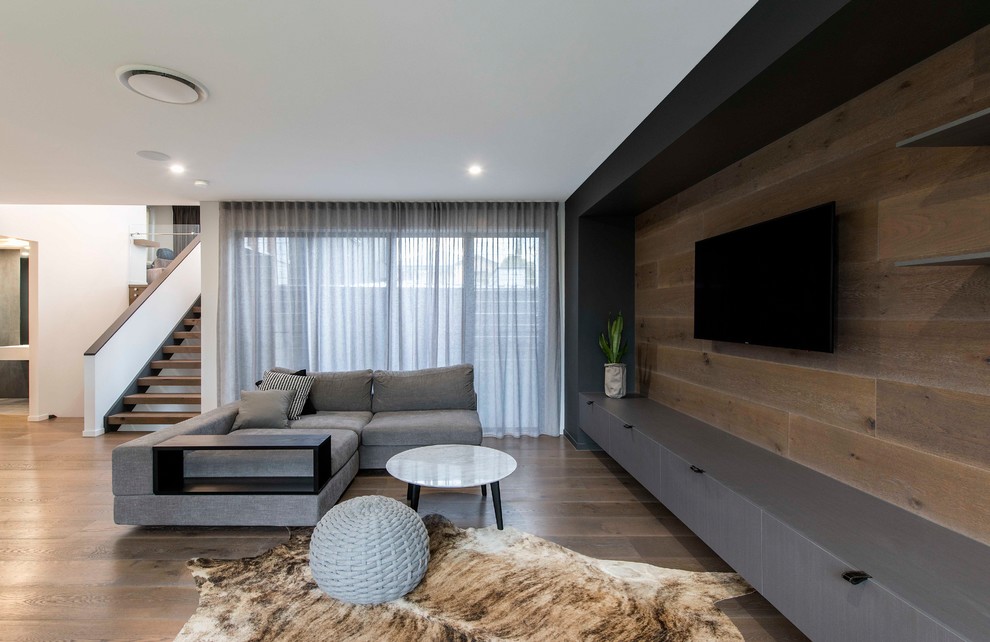 Exempel på ett modernt allrum med öppen planlösning, med vita väggar, en väggmonterad TV, mellanmörkt trägolv och brunt golv