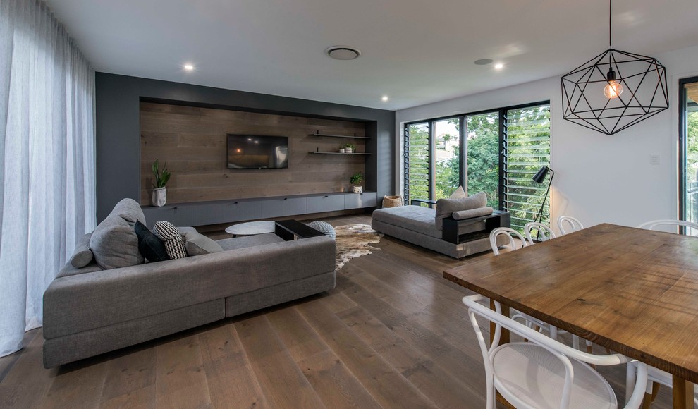 This is an example of a contemporary open plan living room in Brisbane with white walls, a wall mounted tv, medium hardwood flooring, brown floors and feature lighting.