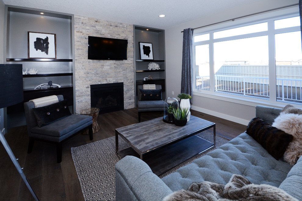 Mittelgroßes, Offenes Klassisches Wohnzimmer mit grauer Wandfarbe, dunklem Holzboden, Kamin, Kaminumrandung aus Stein, TV-Wand und braunem Boden in Calgary
