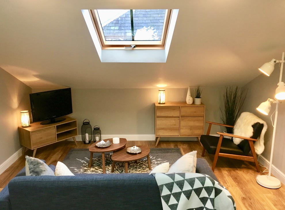 Пример оригинального дизайна: открытая гостиная комната среднего размера в скандинавском стиле с серыми стенами, полом из ламината, отдельно стоящим телевизором и коричневым полом без камина