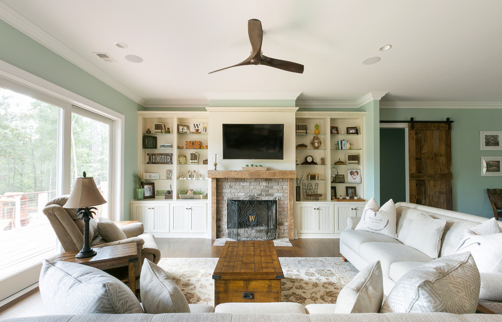 Country formal open plan living room in Charleston with green walls, dark hardwood flooring, a standard fireplace, a brick fireplace surround, a wall mounted tv, brown floors and feature lighting.