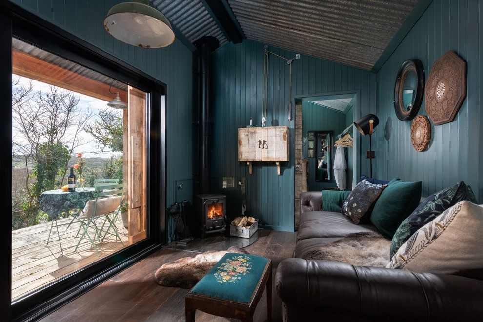 コーンウォールにある小さなラスティックスタイルのおしゃれなLDK (青い壁、濃色無垢フローリング、コーナー設置型暖炉、金属の暖炉まわり、内蔵型テレビ、茶色い床) の写真