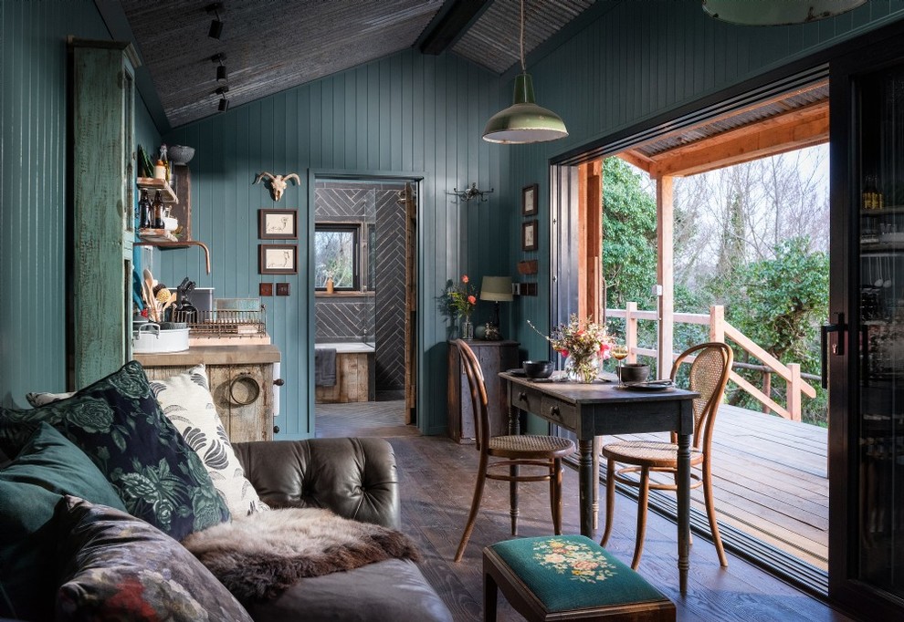 Foto de salón abierto rural pequeño con paredes azules, suelo de madera oscura, chimenea de esquina, marco de chimenea de metal, televisor retractable y suelo marrón