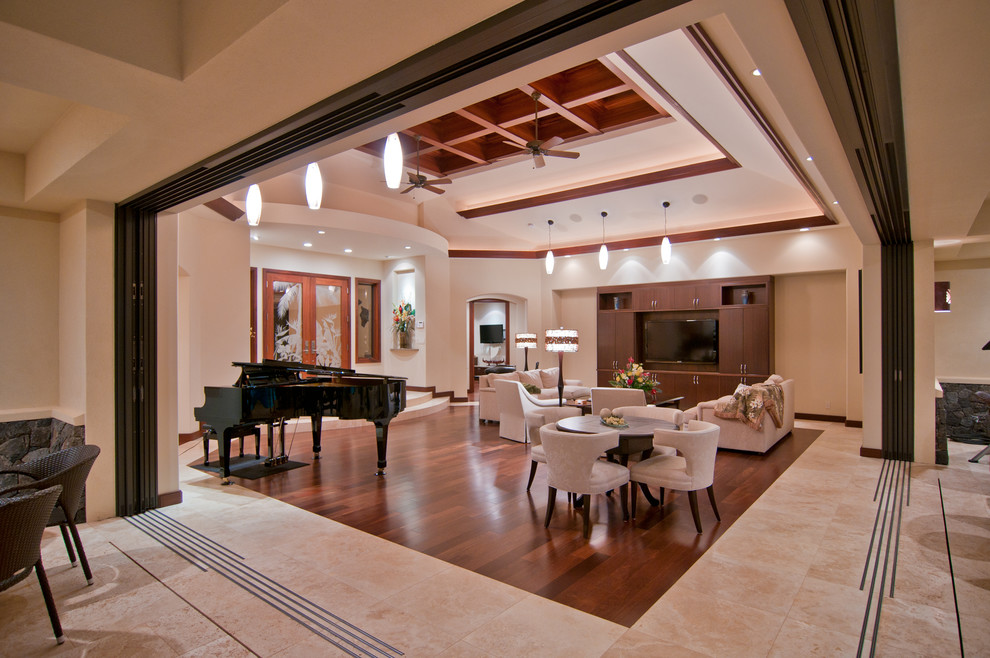 Imagen de salón abierto tropical con suelo de madera en tonos medios y pared multimedia