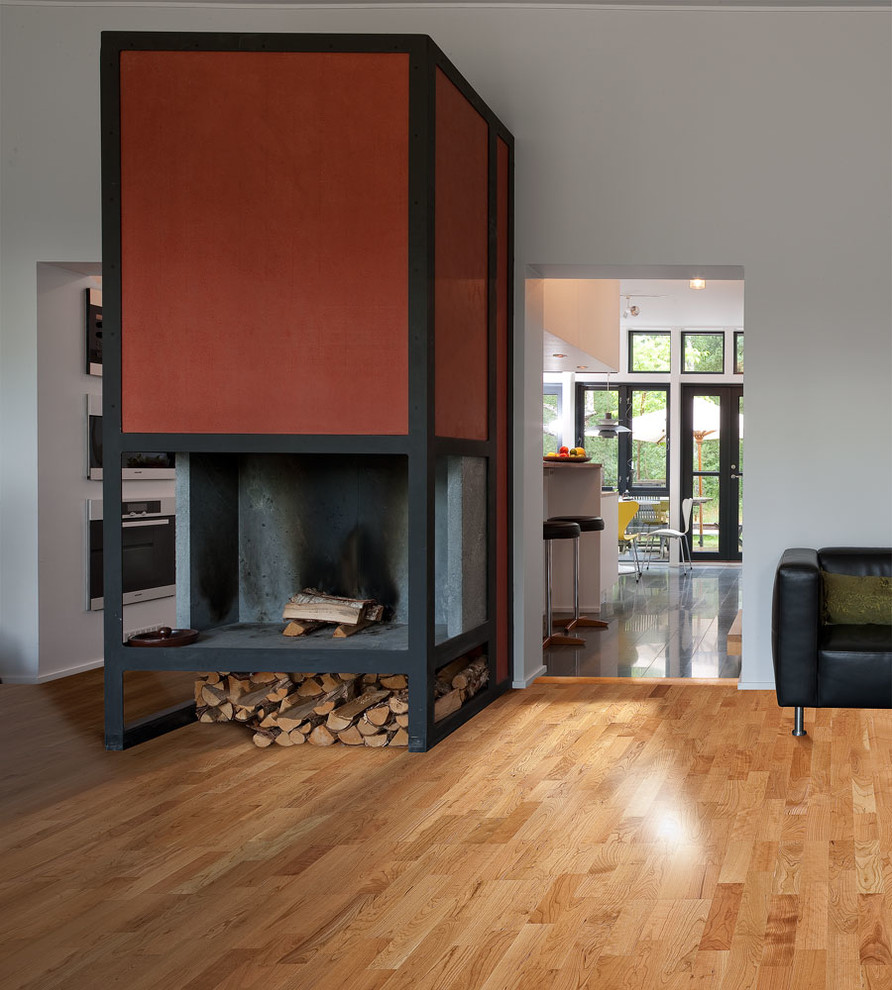 Diseño de salón abierto moderno de tamaño medio con paredes blancas, suelo de madera en tonos medios, chimenea de doble cara y marco de chimenea de metal